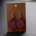 Bright pink teardrop earrings with teal ribbons and stars, one pair