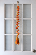Yellow, orange and tan crochet wind spinner with brown stem, decorative picot stitches and tassel hanging against a door.