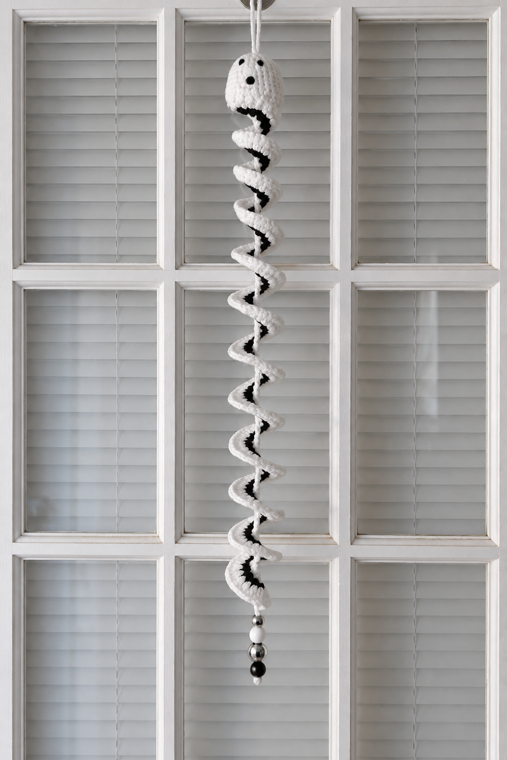 White and black crochet ghost wind spinner with beaded tail hanging against a door.