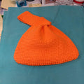 Solid orange hand-crocheted Japanese knot bag with loop strap on a teal background