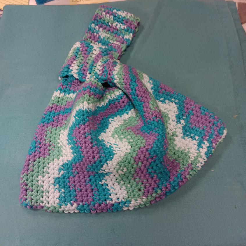 Hand-crocheted Japanese knot bag in teal, purple, green, and cream zigzag colors on a teal background